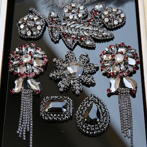 May include: Assortment of black and red rhinestone embellishments with dangling chains. The embellishments are in various shapes, including a leaf, a flower, a star, and a teardrop.