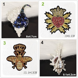 May include: Four embroidered patches: a white and blue beaded shell measuring 8x4.7cm, a red heart with a gold crown measuring 10x9.5cm, a gold sequined bee with a crown measuring 13.5x13cm, and a white beaded shell measuring 9.1x4.2cm.