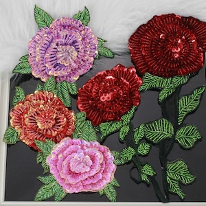 Puede incluir: Cuatro apliques de flores de lentejuelas en tonos rosa, rojo y morado con hojas verdes. Los apliques están hechos de lentejuelas y cuentas y son perfectos para agregar un toque de brillo a cualquier proyecto.