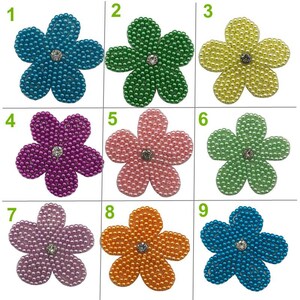 May include: Nine different colored pearl flower embellishments with a rhinestone center. The flowers are arranged in three rows of three. The colors are turquoise, green, yellow, purple, pink, light green, light pink, orange, and blue.