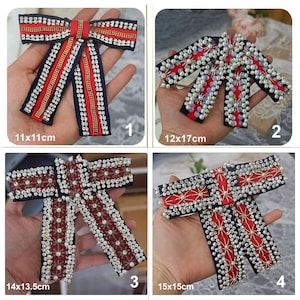 May include: Four decorative bow embellishments with intricate beadwork and embroidery. Each bow features red, navy blue, and white accents. The bows vary in size, with the largest measuring approximately 15 x 15 cm.