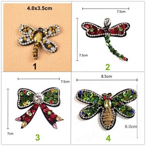 Könnte beinhalten: Vier gestickte Bügelbilder mit einer Libelle, einer Schleife und zwei weiteren Libellen. Die Patches sind mit Pailletten und Strasssteinen verziert. Die Patches sind 4,0 x 3,5 cm, 7,5 cm, 7 cm und 8,5 cm groß.