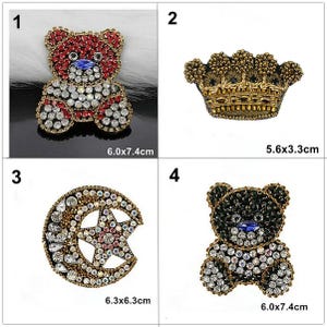 May include: Four bejeweled brooches are displayed. A red and silver teddy bear brooch (6.0 x 7.4 cm), a gold crown brooch (5.6 x 3.3 cm), a crescent moon and star brooch (6.3 x 6.3 cm), and a black and silver teddy bear brooch (6.0 x 7.4 cm).