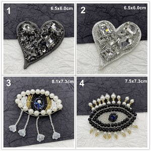 May include: Four embroidered patches with different designs. The first patch is a black heart with rhinestones, measuring 6.5x6.0 cm. The second patch is a silver heart with rhinestones, measuring 6.5x6.0 cm. The third patch is a black and blue eye with white pearls, measuring 8.1x7.3 cm. The fourth patch is a black and blue eye with white pearls, measuring 7.5x7.3 cm.