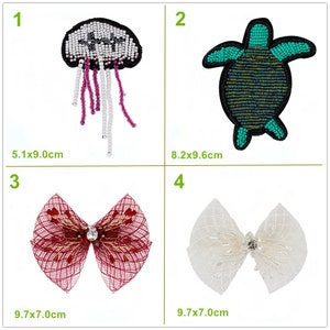 May include: Four different iron-on patches, each with a unique design. The first patch is a white and pink jellyfish with a black outline. The second patch is a green turtle with a black outline. The third patch is a red bow with a rhinestone in the center. The fourth patch is a white bow with a rhinestone in the center.