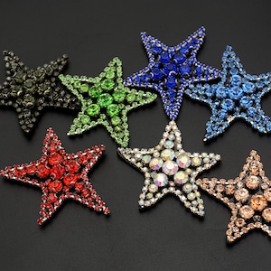 May include: Assortment of six rhinestone starfish in various colors, including red, green, blue, and clear. The starfish are all about 3 inches in diameter and have a silver metal backing.