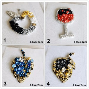 May include: Four beaded brooches in the image. An apple, a wine glass, a leaf with blue gems, and a leaf with gold and black beads. The apple is 6.5 x 5.2 cm. The wine glass is 6.0 x 4.0 cm. The leaves are 7.0 x 4.2 cm.