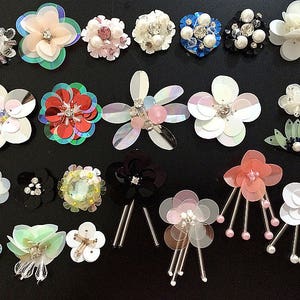 Puede incluir: Surtido de adornos de flores de tela de colores, incluyendo blanco, rosa, rojo, azul y verde. Las flores están hechas de lentejuelas y cuentas, y algunas tienen un efecto 3D.