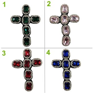 May include: Four different colored cross-shaped embellishments with rhinestones. The crosses are green, pink, red, and blue.