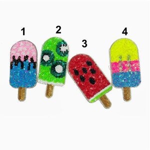 May include: Four colourful popsicle iron-on patches with sequins. The patches are numbered 1 through 4. Patch 1 is pink and blue, patch 2 is green, patch 3 is red and black, and patch 4 is yellow, pink, and blue.