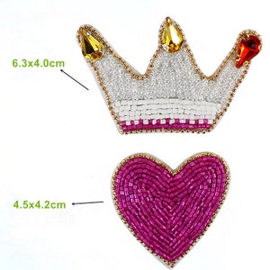Puede incluir: Dos parches de planchado con cuentas, uno una corona blanca con ribetes dorados y piedras de imitación rojas y amarillas, que mide 6,3 por 4,0 cm, y el otro un corazón rosa con ribetes dorados, que mide 4,5 por 4,2 cm.