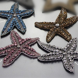 May include: Four bejeweled starfish ornaments in blue, brown, pink, and silver. Each starfish is covered in small, sparkling crystals and features a larger crystal at the centre. These decorative starfish are ideal for embellishing crafts or adding coastal charm.