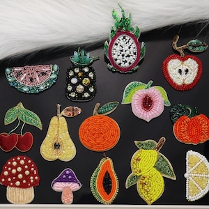 May include: Assortment of colorful beaded fruit and vegetable patches, including a pineapple, watermelon, peach, pear, papaya, lemon, and a dragon fruit. The patches are perfect for adding a touch of whimsy to clothing, bags, or other accessories.