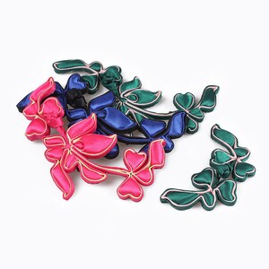 Puede incluir: Surtido de botones de flores de tela de colores en rosa, verde y azul. Los botones tienen forma de flores y hojas, con un nudo decorativo en el centro.