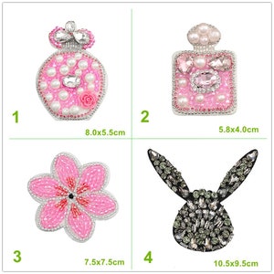May include: Four different rhinestone and pearl embellished iron-on patches. The patches are shaped like a perfume bottle, a flower, a bunny, and a square perfume bottle. The patches are all pink and white except for the bunny, which is black and silver.