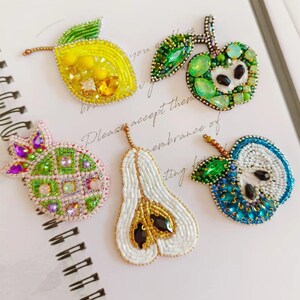 May include: Five beaded fruit brooches, including a lemon, pear, pineapple, apple, and green apple. The brooches are made with colourful beads and sequins.