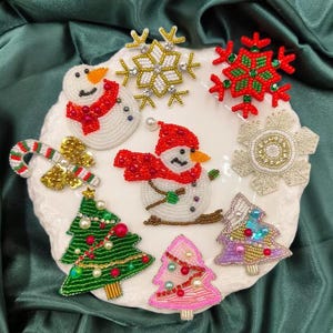 May include: A collection of beaded Christmas ornaments, including a snowman, a candy cane, a Christmas tree, and snowflakes. The ornaments are all white with colorful accents.