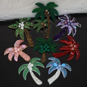 May include: A collection of beaded palm tree embellishments in various colors. The designs include green, pink, red, purple, and blue palm trees with detailed beadwork. The palm tree trunks are brown and gold, and the leaves are green.