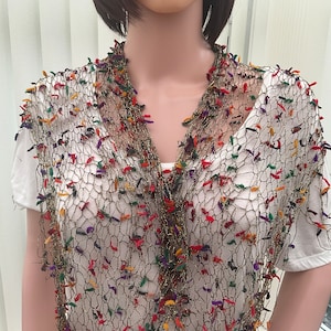 May include: A gold mesh scarf with colorful yarn accents. The scarf is draped over a white shirt on a mannequin.