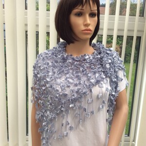 May include: A light blue crocheted shawl with a fringe. The shawl is draped over a white shirt on a mannequin.