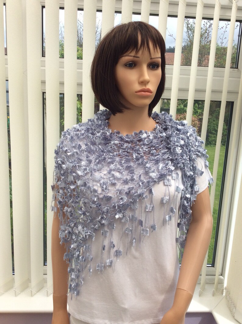 May include: A light blue crocheted shawl with a fringe. The shawl is draped over a white shirt on a mannequin.