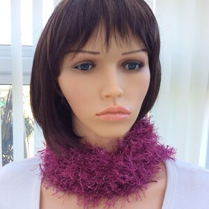 May include: A close-up of a mannequin wearing a pink fuzzy neck warmer. The neck warmer is made of a soft, fluffy material and has a loose, flowing design.