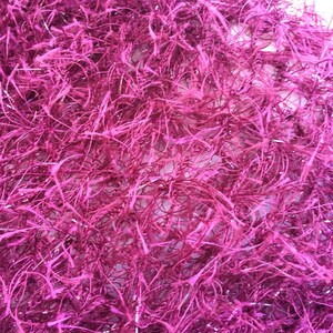 May include: A close-up of a pink, fluffy, sparkly material. The material is made of thin, interwoven strands that create a soft, textured surface.