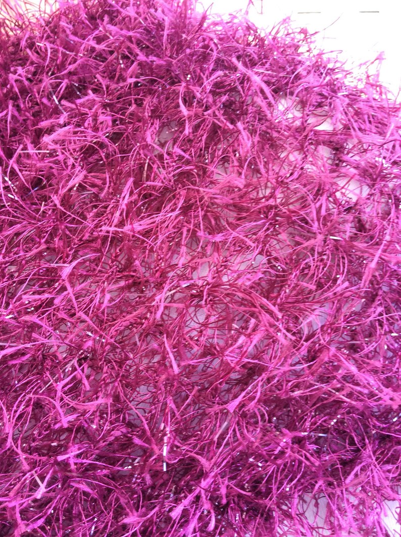 May include: A close-up of a pink, fluffy, sparkly material. The material is made of thin, interwoven strands that create a soft, textured surface.