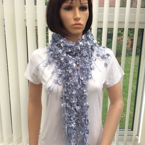 May include: A light blue crocheted scarf with a frayed texture. The scarf is draped around a mannequin's neck.