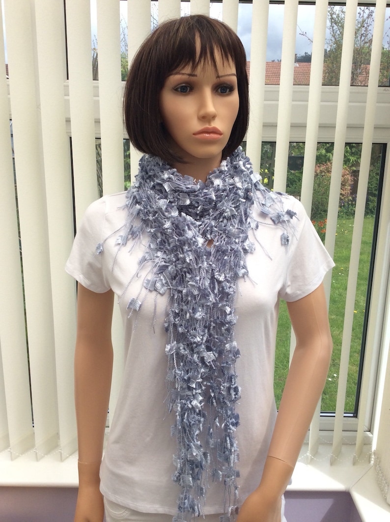 May include: A light blue crocheted scarf with a frayed texture. The scarf is draped around a mannequin's neck.