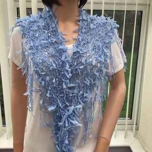 Peut inclure: Une &eacute;charpe en crochet bleu clair avec des franges. L'&eacute;charpe est drap&eacute; sur les &eacute;paules d'un mannequin.