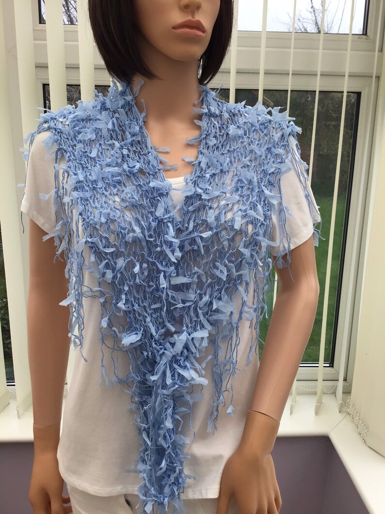 Peut inclure: Une &eacute;charpe en crochet bleu clair avec des franges. L'&eacute;charpe est drap&eacute; sur les &eacute;paules d'un mannequin.