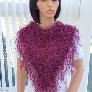 May include: A deep purple fuzzy shawl with a triangular shape and long fringe. The shawl is worn by a mannequin with short dark hair.
