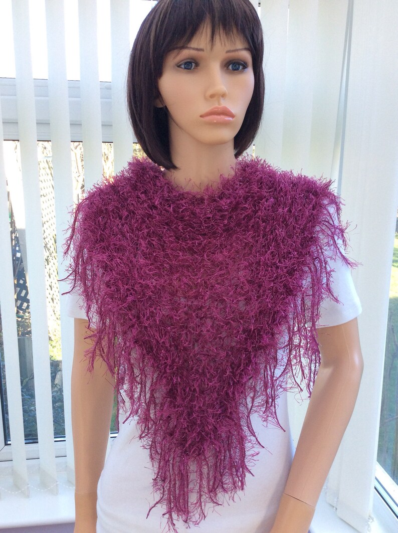 May include: A deep purple fuzzy shawl with a triangular shape and long fringe. The shawl is worn by a mannequin with short dark hair.