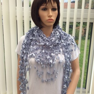 May include: A light blue crocheted scarf with a delicate, lacy design and fringe. The scarf is draped around the neck of a mannequin.