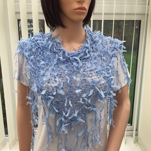 Peut inclure: Un ch&acirc;le en crochet bleu clair avec une bordure en franges. Le ch&acirc;le est drap&eacute; sur les &eacute;paules d'un mannequin.