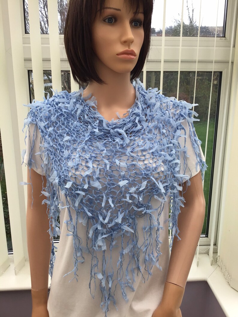 Peut inclure: Un ch&acirc;le en crochet bleu clair avec une bordure en franges. Le ch&acirc;le est drap&eacute; sur les &eacute;paules d'un mannequin.