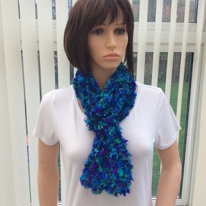 May include: A blue and green fuzzy scarf with a fluffy texture. The scarf is tied around the neck of a mannequin.