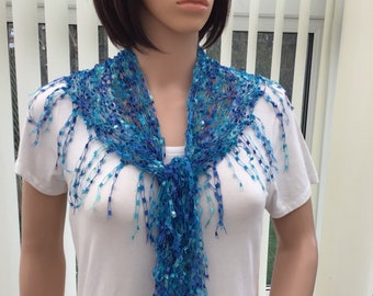 May include: A blue and turquoise crocheted scarf with fringe. The scarf is tied around the neck of a mannequin.