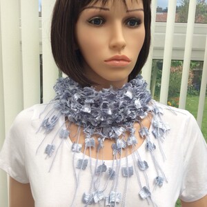May include: A light blue crocheted scarf with fringe. The scarf is worn around the neck of a mannequin.