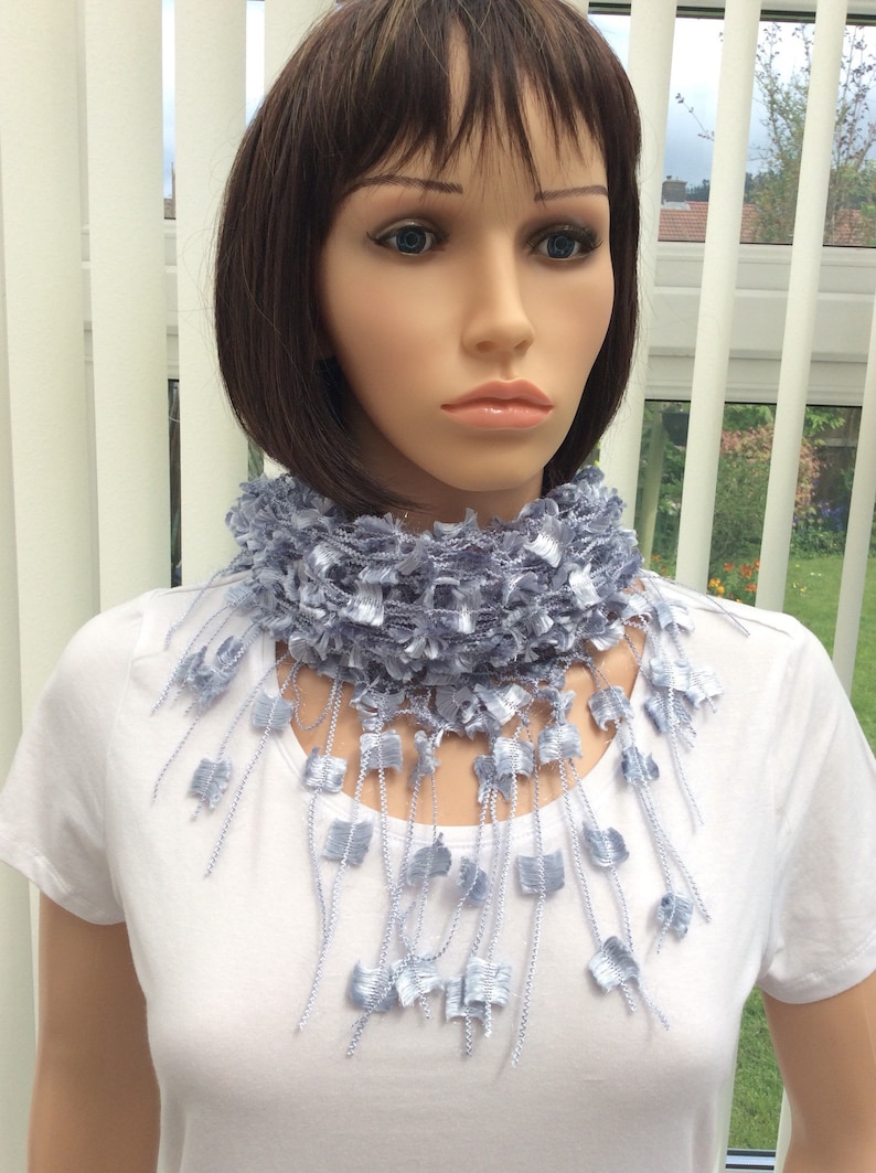 May include: A light blue crocheted scarf with fringe. The scarf is worn around the neck of a mannequin.