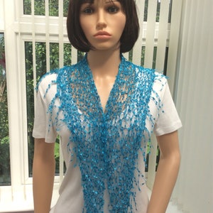 Könnte beinhalten: Ein türkisfarbener Häkel-Schal mit Fransen. Der Schal ist um den Hals einer Schaufensterpuppe gelegt.