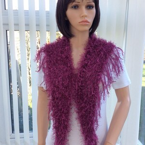 May include: A long, purple, fuzzy scarf with fringe. The scarf is draped around a mannequin's neck.