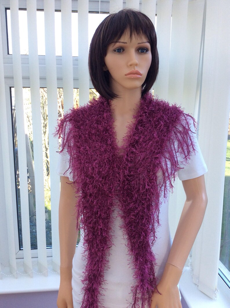 May include: A long, purple, fuzzy scarf with fringe. The scarf is draped around a mannequin's neck.