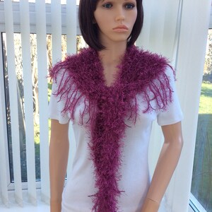 May include: A long, purple, fuzzy scarf with fringe. The scarf is draped around the neck of a mannequin.