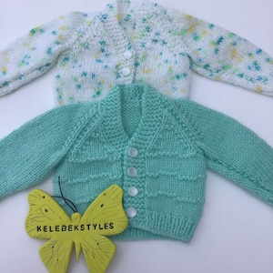 May include: Two knitted baby cardigans, one white with green and yellow speckles and one light green with a button closure. A yellow butterfly with the text "KELEBEKSTYLES" is in the foreground.
