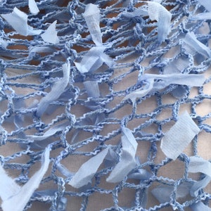 Peut inclure: Une &eacute;charpe en crochet bleu clair avec un motif en filet et des bords effiloch&eacute;s. L'&eacute;charpe est faite d'un mat&eacute;riau doux et l&eacute;ger et a une sensation d&eacute;licate et a&eacute;r&eacute;e.