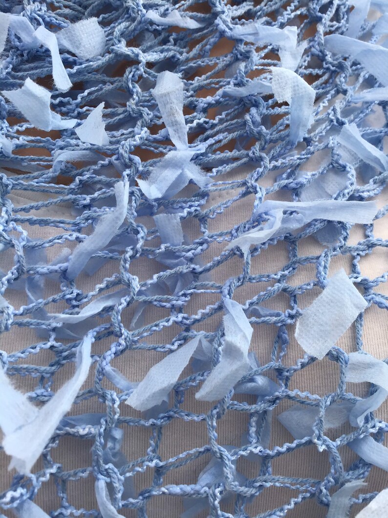 Peut inclure: Une &eacute;charpe en crochet bleu clair avec un motif en filet et des bords effiloch&eacute;s. L'&eacute;charpe est faite d'un mat&eacute;riau doux et l&eacute;ger et a une sensation d&eacute;licate et a&eacute;r&eacute;e.