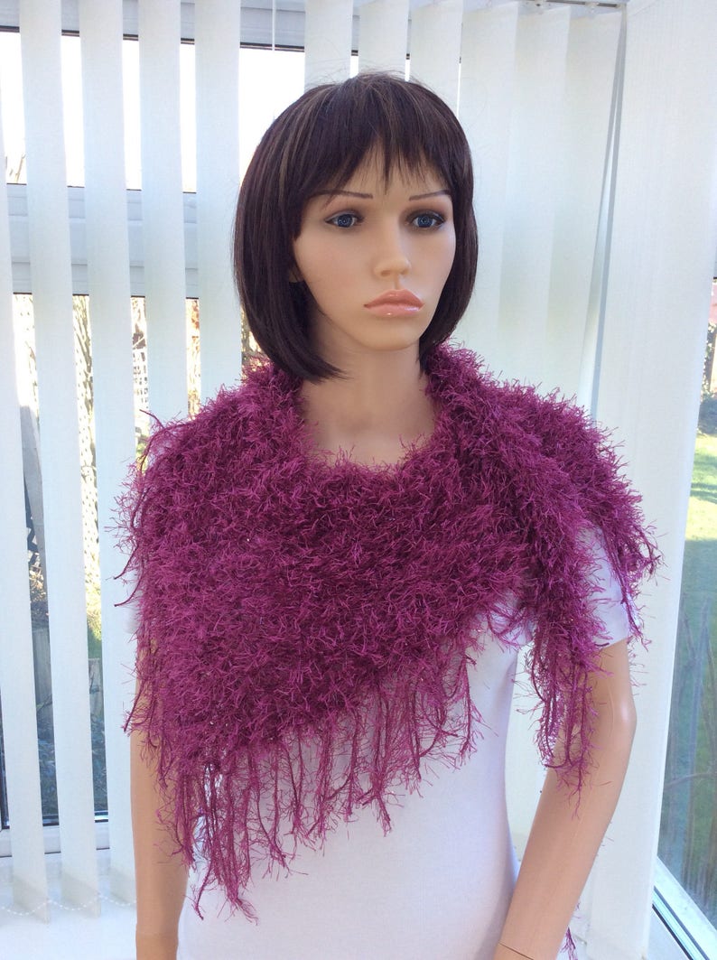 May include: A magenta fuzzy knit scarf with fringe. The scarf is draped around a mannequin's neck.