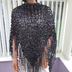 May include: Black crochet poncho with fringe detail. The poncho is made from a lightweight, open-weave fabric.